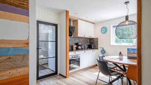A modern kitchen with a dining area, wooden flooring, and a large window with a view.
