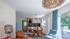 A modern living room with a dining area, a kitchen, and a large sliding glass door leading to an outdoor patio.