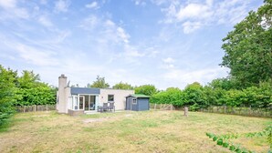 A modern house with a large backyard, a fenced garden, and a clear sky.