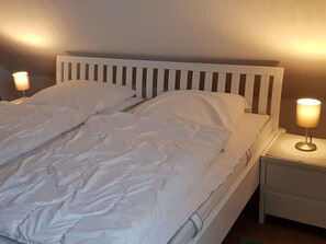 A neatly made bed with white bedding and two bedside lamps on white nightstands. - Holiday Apartment Bathmann (Cuxhaven)