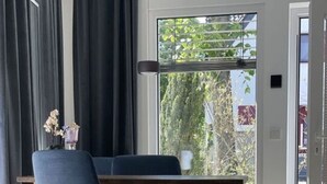 A dining area with a table and chairs, a window with a view of greenery, and a door leading outside. - Sartoris Comfortable Holiday Residence (Bad Neuenahr-Ahrweiler)