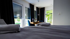 A hotel room with a large bed, a desk with a chair, and a view of greenery outside. - Sartoris Comfortable Holiday Residence (Bad Neuenahr-Ahrweiler)