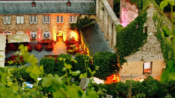 A stone building with a courtyard, featuring a large archway and a dining area with tables and umbrellas. - Sartoris Comfortable Holiday Residence (Bad Neuenahr-Ahrweiler)