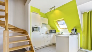 Une cuisine avec des meubles blancs, un four encastré, un micro-ondes et un petit îlot central doté d’un évier.