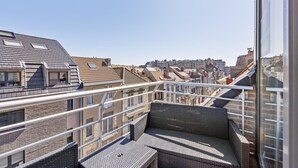 Un balcon doté de meubles en osier, une vue dégagée sur le paysage urbain et un bâtiment moderne à la façade en verre.