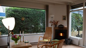 Una habitació acollidora amb una llar de foc, cadires de vimet, una taula amb espelmes i vistes a la verdor exterior.