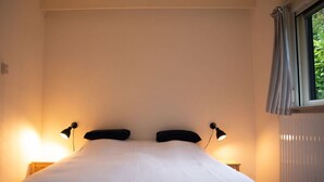 Un dormitori amb un llit gran, dues làmpades de nit, un radiador i una finestra amb cortines.