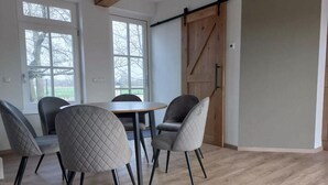 Un coin repas avec une table en bois et six chaises, de grandes fenêtres et une porte de style grange.