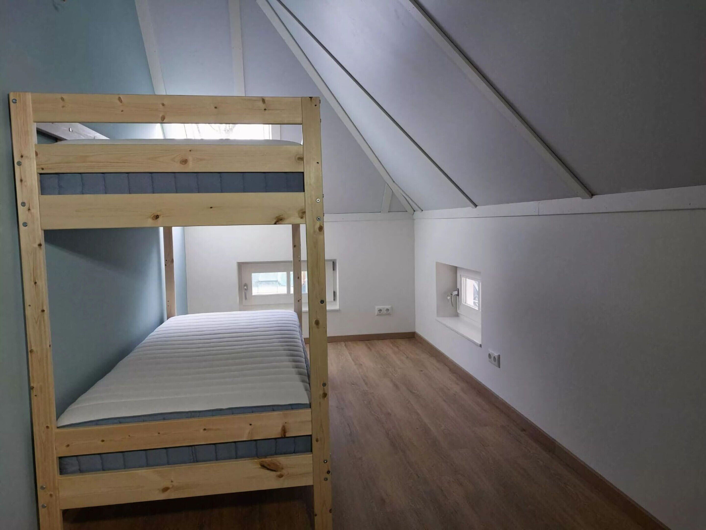 A bunk bed in a room with a sloped ceiling, a small window, and a wall-mounted light fixture.