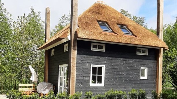 Une maison en bois avec un toit de chaume, un petit porche et une fenêtre.