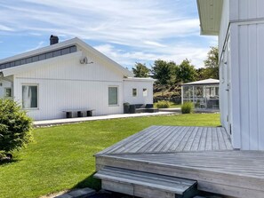 Uma casa moderna com um amplo deck, área externa coberta e gramado bem cuidado.