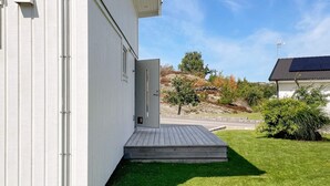 Een wit gebouw met een houten terras en een deur die uitkomt op een grasveld.
