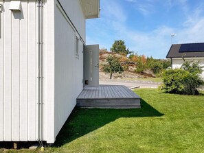 Um edifício branco com deck de madeira e porta que dá para uma área gramada.