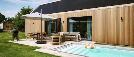 A modern house with a swimming pool, outdoor furniture, and a barbecue grill.