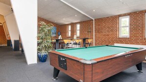 Ein Billardtisch in einem Raum mit Backsteinwänden, einer Topfpflanze und einem Fenster.