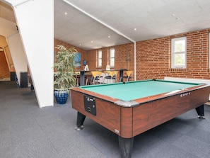 Une table de billard dans une pièce aux murs en briques, avec une plante en pot et une fenêtre.