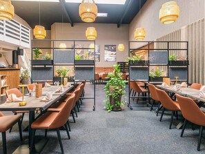 Een moderne eetruimte met lange tafels, bruine stoelen en hangende rieten lampen.