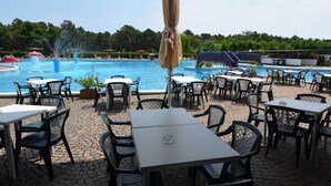 An outdoor pool area with tables and chairs, a fountain, and a view of the pool. - Bungalow in Italy Near Beach & Water Park (Ravenna)