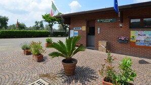 A building with a reception area, a sign for 'Reception Change', and a flagpole with flags. - Bungalow in Italy Near Beach & Water Park (Ravenna)