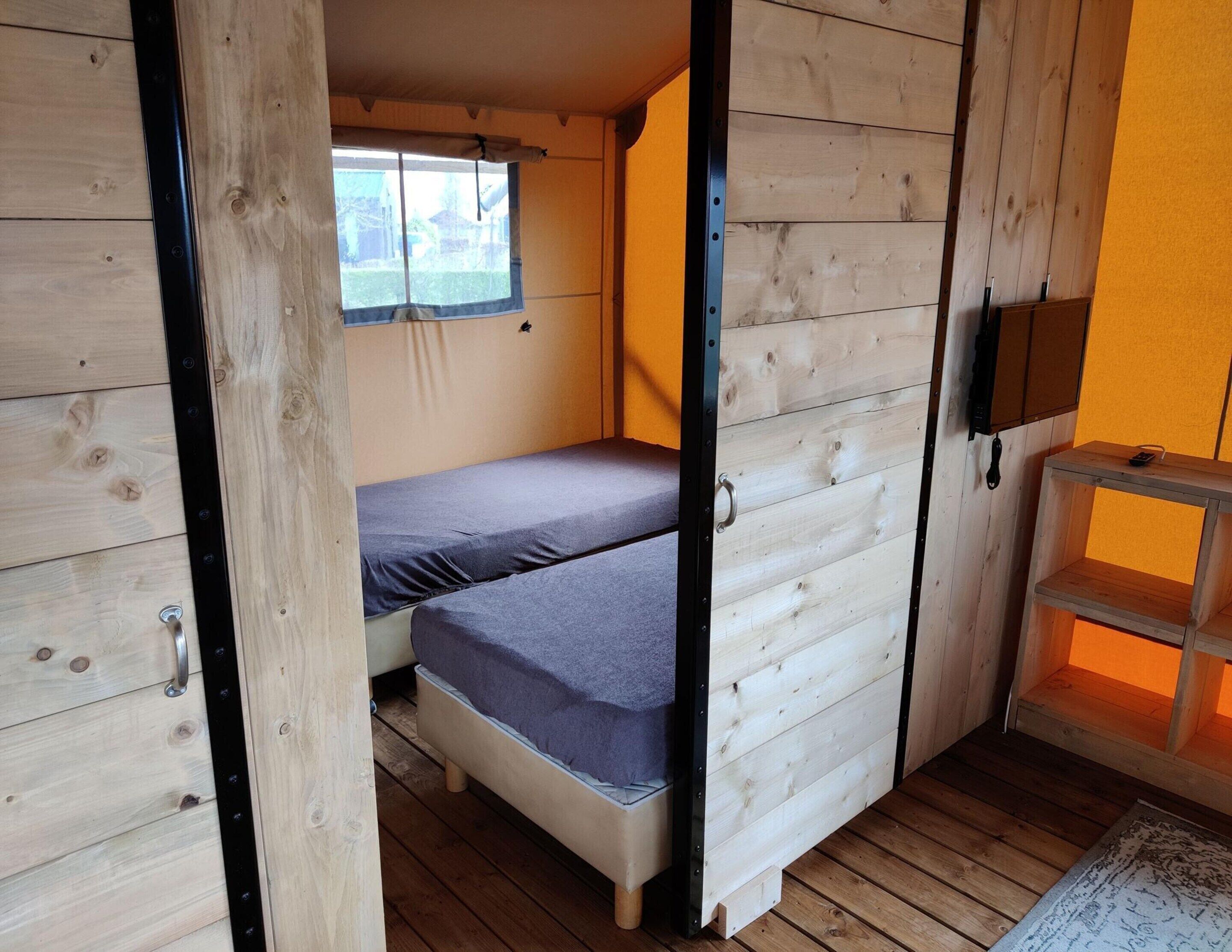 Ein kleines Zimmer mit zwei Betten, einem Fenster und einer kleinen Holzablage.