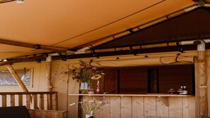 Une terrasse en bois avec une table d’échecs, un canapé et une étagère ornée de fleurs et de bouteilles.