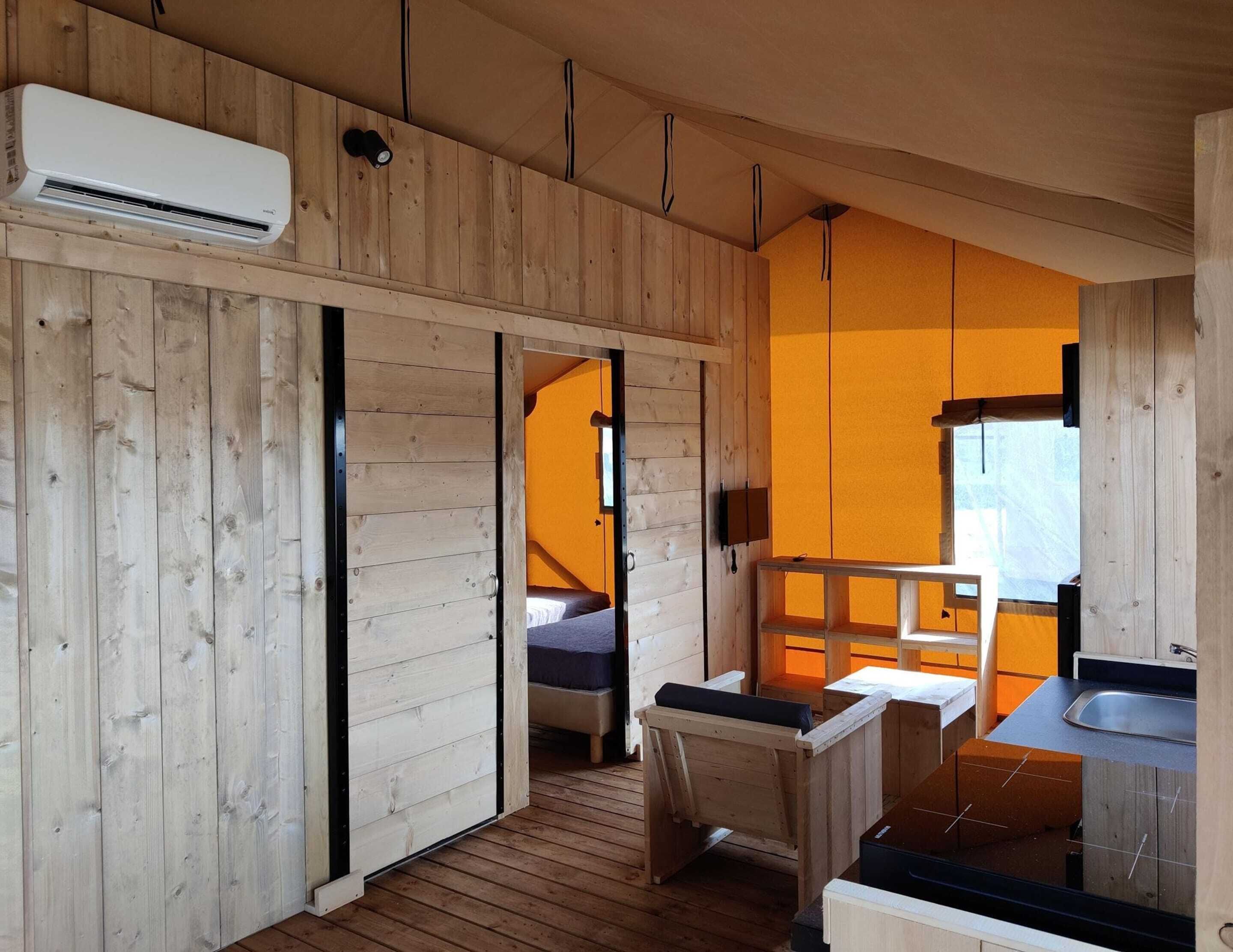 A wooden cabin interior with a bed, a small kitchenette, and a bathroom.