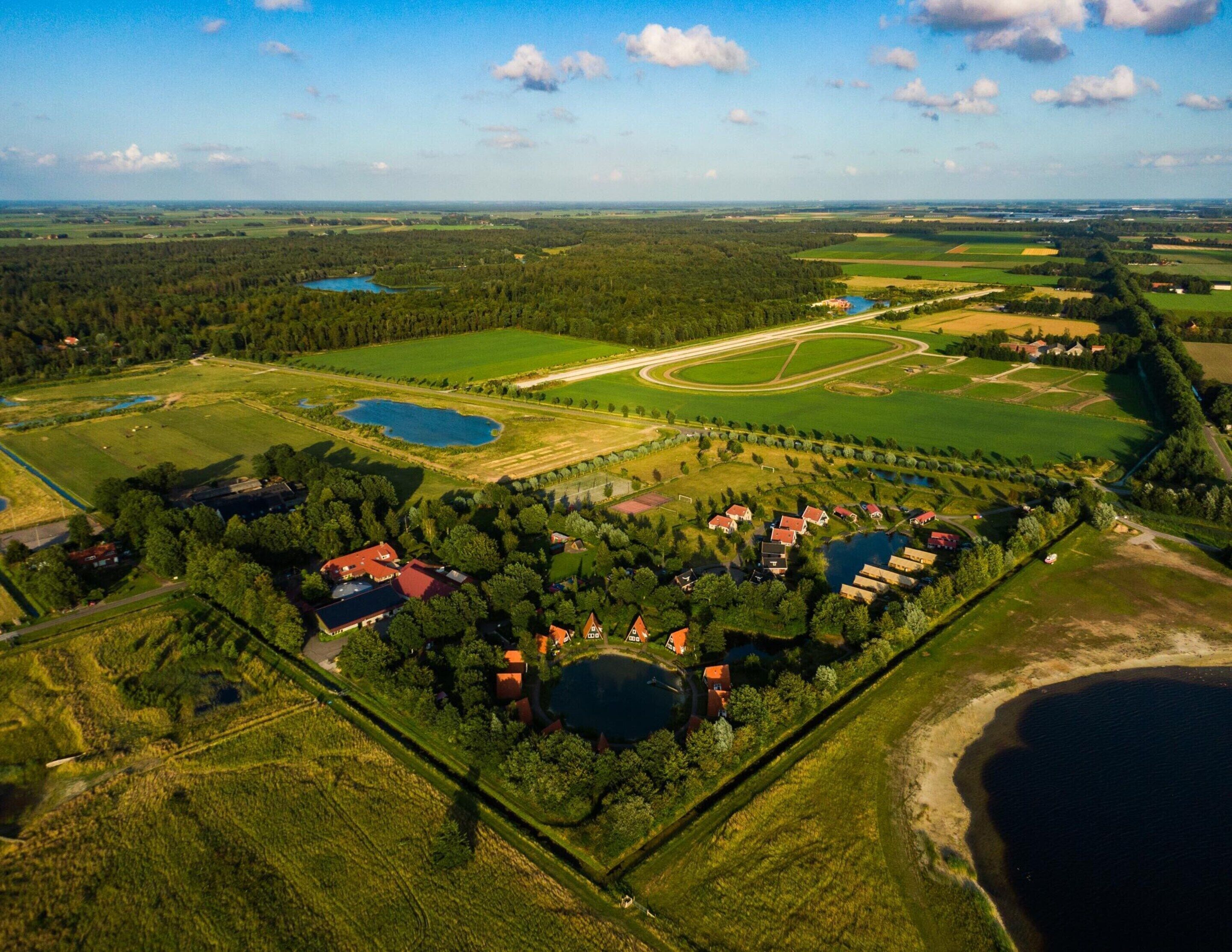 Vista aérea de una zona rural con campos, un lago y un grupo de casas con tejados rojos.