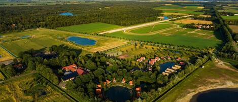 Vista aérea de una zona rural con campos, un lago y un grupo de casas con tejados rojos.
