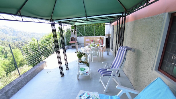 Ein überdachter Außenbereich mit Lounge-Möbeln und einem Tisch, mit Blick auf eine gebirgige Landschaft.