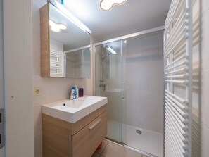 Une salle de bain moderne avec un meuble-lavabo blanc, une cabine de douche en verre et un porte-serviettes.