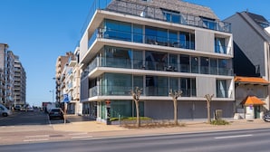 Een modern meerlaags gebouw met grote ramen en balkons, gelegen aan een kustweg.