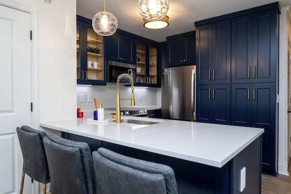 A modern kitchen with dark blue cabinets, a stainless steel refrigerator, and a white island with bar stools.