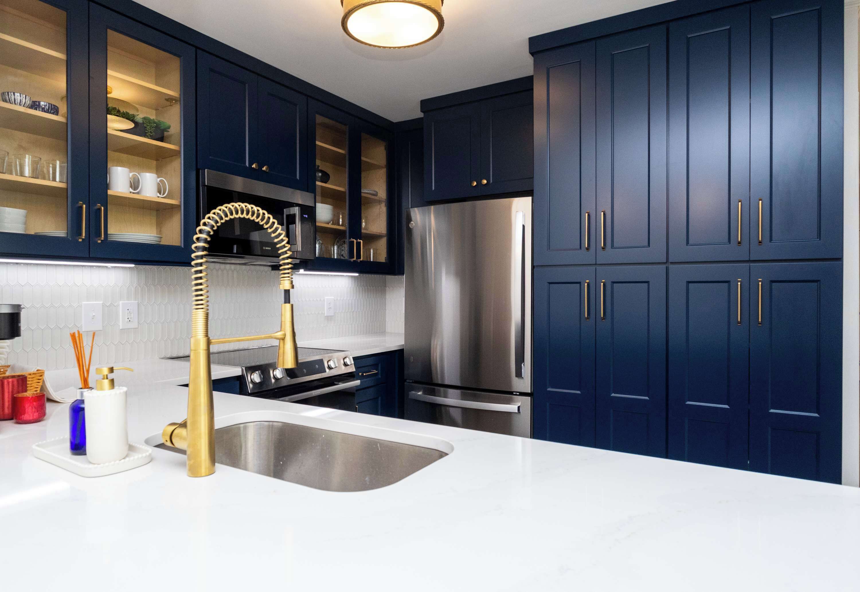 A modern kitchen with dark blue cabinets, stainless steel appliances, and a gold faucet.