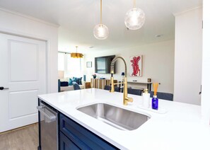 A modern kitchen with a white countertop, stainless steel sink, and gold faucet.