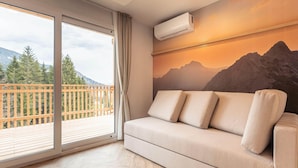 A room with a sofa, an air conditioning unit, a large window with a view of mountains, and a wooden deck outside. - Beautiful Tree House in the Gailtal Valley (Kotschach-Mauthen)