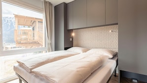 A modern bedroom with a large bed, a view of a wooden deck, and a patterned headboard. - Beautiful Tree House in the Gailtal Valley (Kotschach-Mauthen)