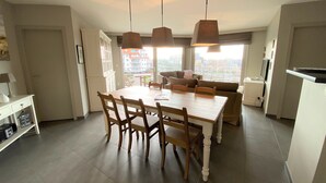 Una cocina moderna con una mesa de comedor, sillas e iluminación colgante. Se ve la ciudad a través de amplios ventanales.