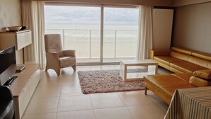 A modern hotel room with a large sliding glass door to the balcony, a sofa, a coffee table, and a TV. - Apartment in Nieuwpoort by the Beach (Nieuwpoort)