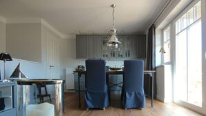 A modern kitchen with grey cabinets, a dining area with two chairs, and a large window providing natural light. - Captain House Wangerooge - Nautik Suite (Wangerooge)