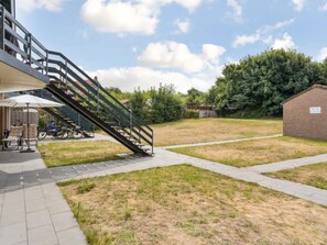 Un espace patio avec un escalier menant à un bâtiment, des sièges extérieurs et une pelouse.