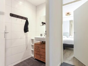 Une salle de bain moderne avec des carreaux blancs, un meuble-lavabo en bois, un porte-serviettes et un miroir.