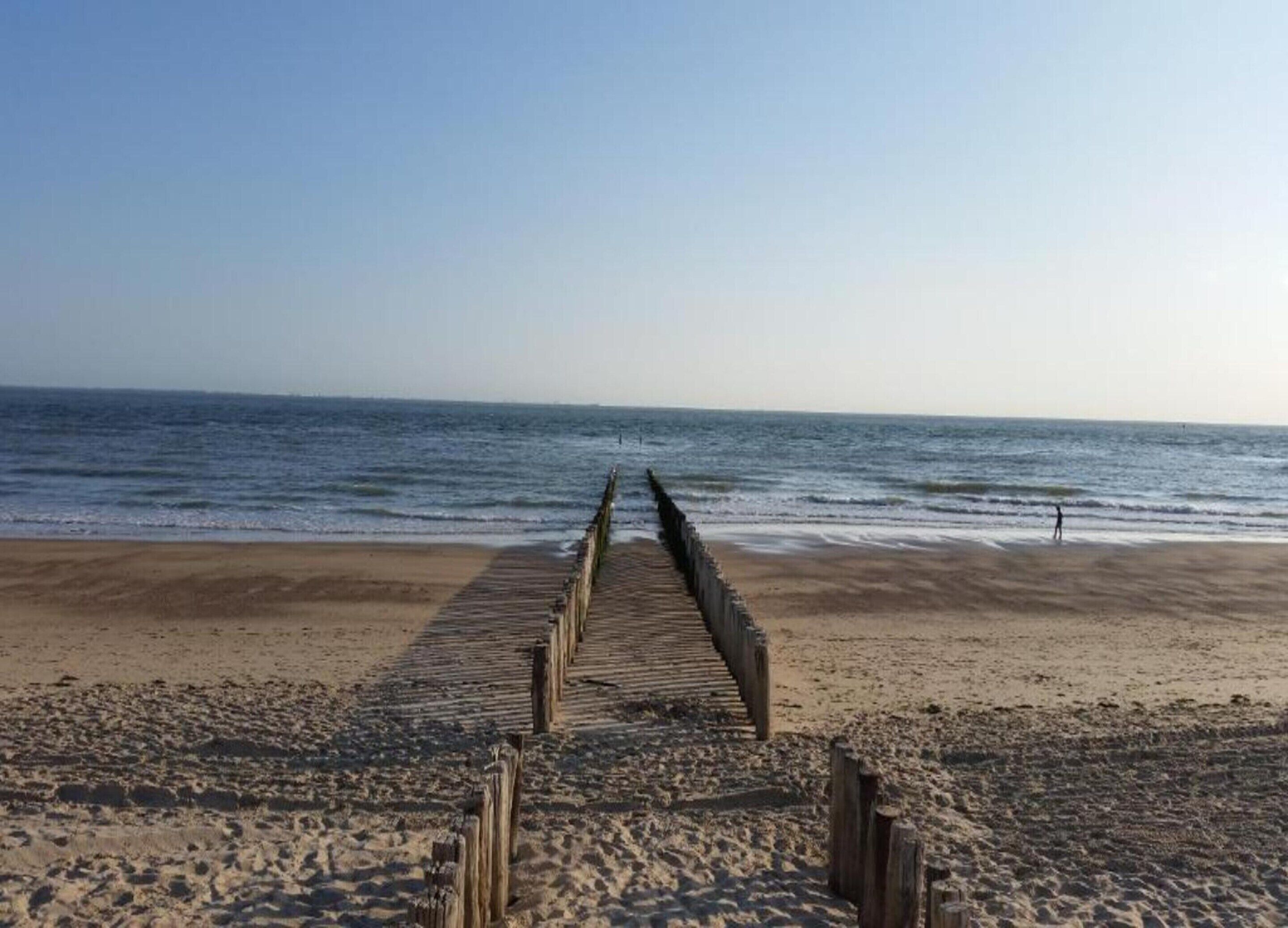 Ein hölzerner Steg führt zu einem Strand mit freiem Blick auf den Ozean.