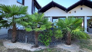 A modern two-story house with a white exterior and dark roof, surrounded by a stone wall and palm trees. - Regal Apartment in Pracht With Garden and Grill (Pracht)
