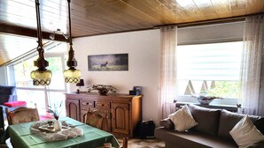 A cozy living room with a dining table, wooden chairs, a sofa, and a cabinet. - Regal Apartment in Pracht With Garden and Grill (Pracht)