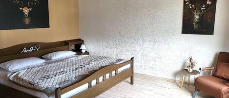 A bedroom with a wooden bed, a small bedside table with a lamp, a decorative pillow, and a rug.