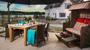 Un espace de restauration en plein air comprenant une table et des chaises, un grand parasol et un fauteuil de jardin en osier avec des coussins.