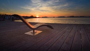 Une jetée en bois avec un banc donnant sur une étendue d’eau au coucher du soleil.