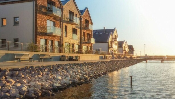Une propriété située au bord de l’eau, avec des bâtiments modernes, un mur de soutènement en pierre et une rivière paisible.