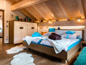A bedroom with a wooden ceiling, a bed with blue and white bedding, a white wardrobe, and a fluffy white rug. - Apartment in Garmisch-partenkirchen (Garmisch-Partenkirchen)