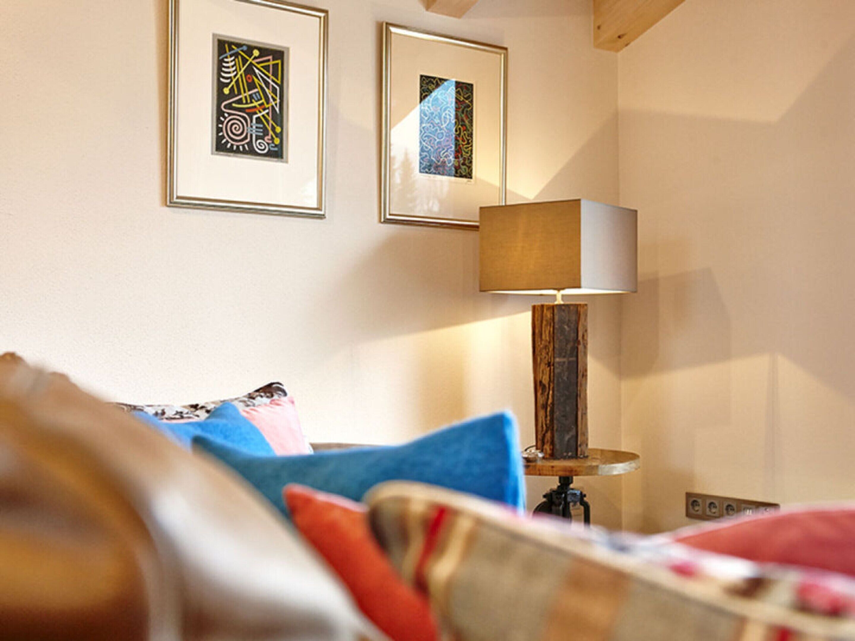 Ein Schlafzimmer mit einem Bett, Kissen, einer Lampe und zwei gerahmten Kunstwerken an der Wand.